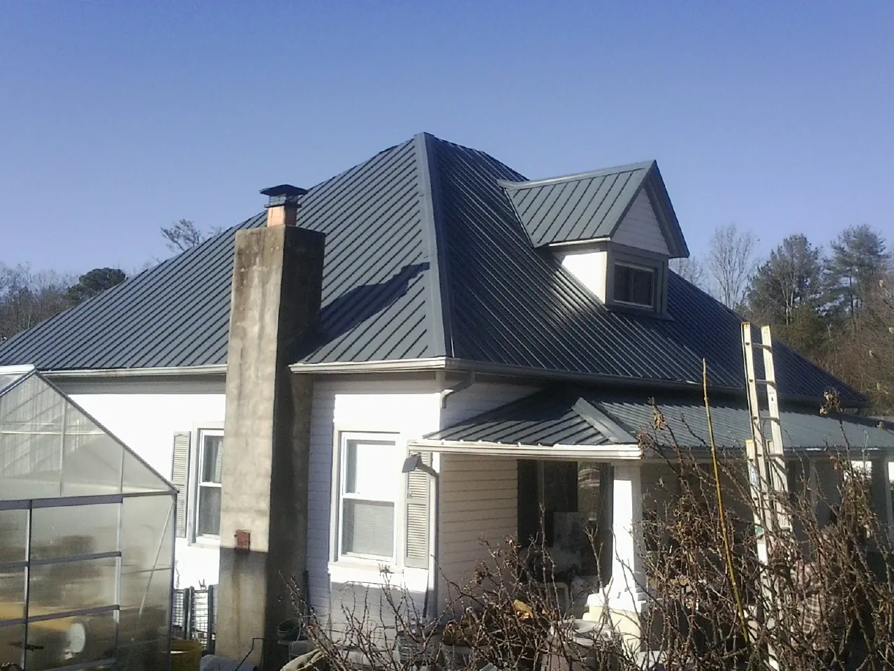 Dark blue standing seam metal roof on a white farmhouse with dormer — Slate & Tile Roof Repair by Roofing Brothers in Barclay