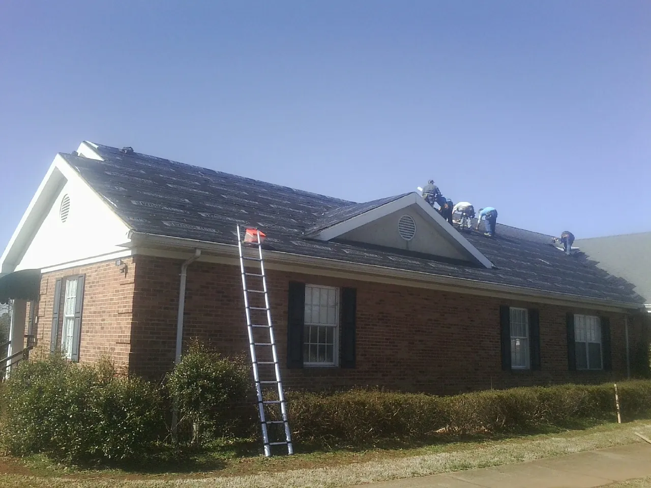 Crew tearing shingles off a brick ranch roof with a ladder set — Emergency Roof Repair work by our crew in Barclay
