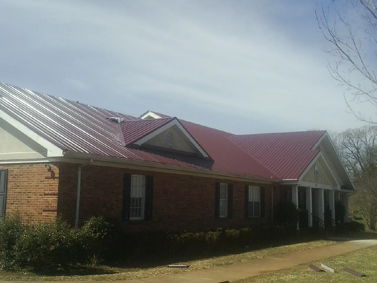Red metal roof with gabled entries on a long brick building, from a Hail Damage Roof Repair job in Barclay