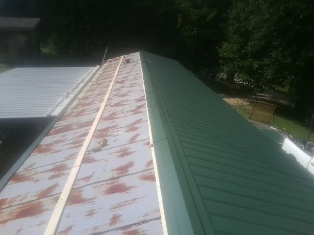 Old rusted panels beside newly installed green metal roofing — Wind Damage Roof Repair by Roofing Brothers in Barclay