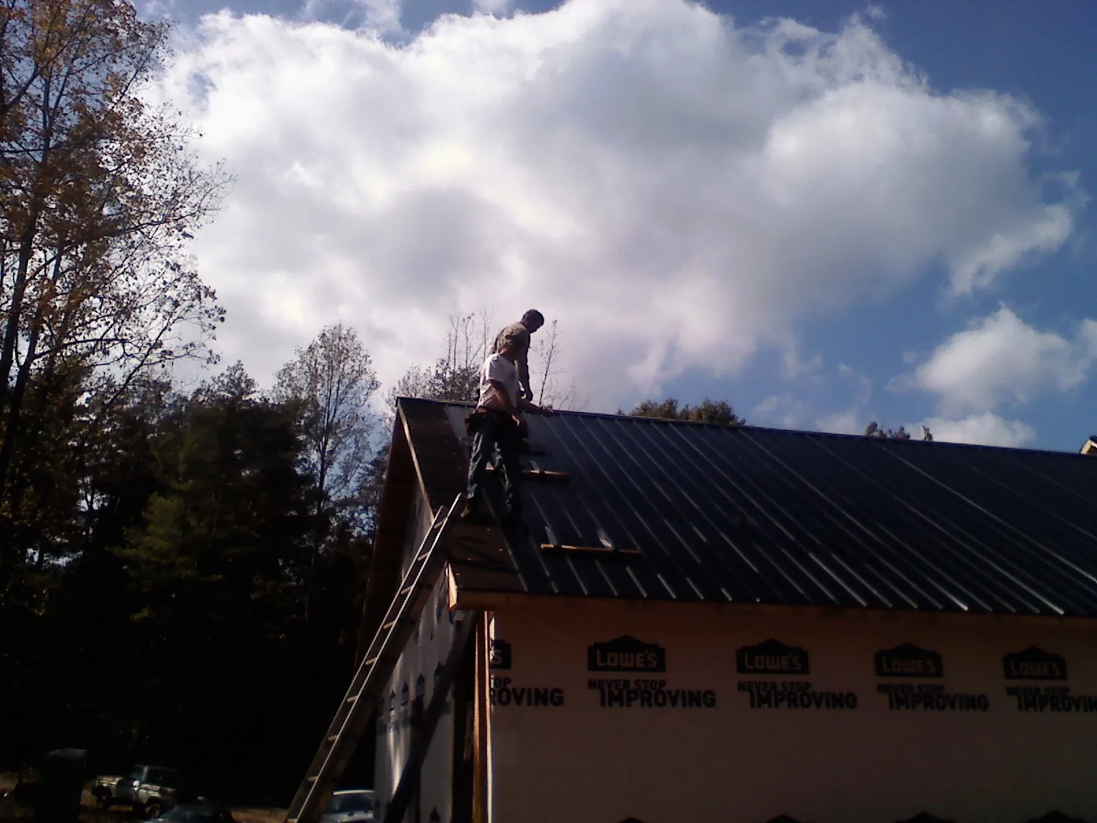 Roofer fastening dark metal panels high against a cloudy sky, from a Roof Inspection job in Barclay