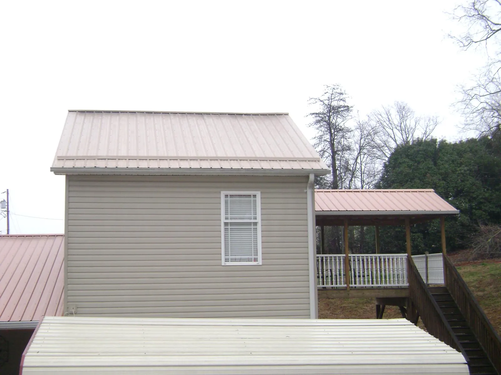 Tan metal roofs on a two story addition and attached porch, from a Roof Replacement job in Barclay